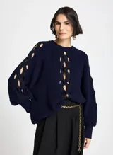 Sweater de punto color azul marino con diseño de aberturas entrelazadas en el frente y a lo largo de las mangas. Presenta cuello redondo, mangas largas con puños ajustados y un corte holgado.