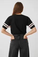 Remera de algodón de corte holgado con cuello redondo y mangas cortas. Presenta un diseño de estilo deportivo con franjas blancas en las mangas y una estampa frontal con temática de béisbol y un tigre.