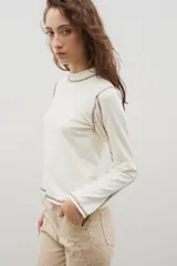 Remera de cuello alto y manga larga en color crudo, con costuras a la vista en contraste de color marrón.