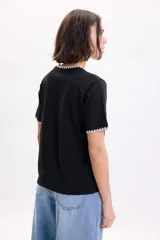 Camiseta de manga corta negra con detalles de pespuntes blancos en contraste en el cuello redondo y en los bordes de las mangas.