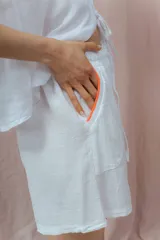 Short blanco de calce relajado con cintura elástica y lazo regulable. Presenta bolsillos amplios con ribete interior de color naranja neón.