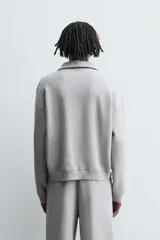 Polo de punto de corte relajado, confeccionado en mezcla de algodón, con cuello solapa, cierre frontal de cremallera y manga larga con acabados en rib.