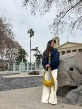 Cartera tipo hobo de cuero gamuzado color verde oliva, con cierre superior y correa ajustable. Presenta una etiqueta de cuero con el logo de la marca en el frente.