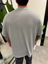 Remera de corte oversize confeccionada en tejido de punto con textura tipo waffle, color gris oscuro, con cuello redondo y mangas cortas.