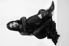 Vestido largo de encaje negro con transparencias, corte ajustado al cuerpo, mangas largas con terminación acampanada y falda con caída fluida.