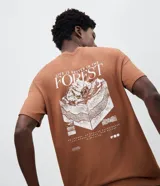 Remera de algodón color marrón con cuello redondo y mangas cortas. Presenta una estampa gráfica en la espalda con un diseño de paisaje montañoso y tipografía en color blanco.