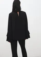 Blusa negra de cuello alto con cierre de botones, diseño recto y mangas largas acampanadas con volantes en los puños. Confeccionada en tejido fluido.