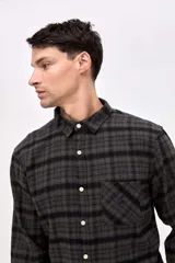 Camisa de corte regular fit, confeccionada en tela de algodón con diseño de cuadros en tonos marrones y negros. Presenta cuello clásico, cierre frontal con botones personalizados y un bolsillo en el pecho con el logo de la marca bordado.