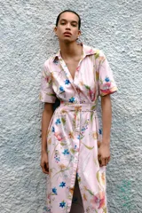 Vestido midi de corte camisero con estampado floral multicolor sobre fondo rosa claro. Presenta cuello solapa, manga corta, cierre frontal con botones y cinturón del mismo tejido con hebilla forrada.