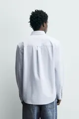 Camisa de corte regular fit confeccionada en tejido de algodón con diseño de rayas verticales. Presenta cuello abotonado, manga larga con puños abotonados, bolsillo plastrón en el pecho y cierre frontal con botones.