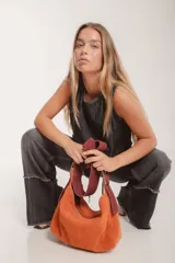 Bolso tipo hobo de gamuza color naranja quemado, con correa ancha de tela color bordó.