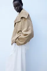 Cazadora bomber marrón de efecto gamuza, con cuello de solapa amplia, manga larga, bolsillos delanteros y cierre frontal asimétrico con cremallera metálica.