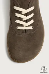 Zapatilla deportiva barefoot fabricada en piel con acabado serraje de color marrón, con cordones en contraste y suela fina de goma.