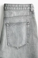 Jean de cinco bolsillos en denim de algodón rígido, de corte holgado estilo baggy, con piernas rectas y tiro alto. Presenta efecto deslavado y cierre con botón y cremallera.
