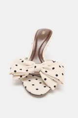 Sandalia tipo mule color crema con estampado de lunares negros, detalle de lazo en la parte delantera, tacón fino alto y punta fina.