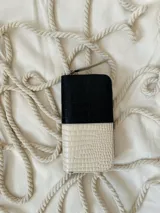 Billetera grande de cuero con diseño bicolor en negro y beige, con textura grabada tipo cocodrilo. Cuenta con cierre metálico perimetral y tirador de cuero.