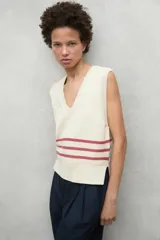Chaleco de punto color crema con cuello en V, sin mangas y aberturas laterales en el ruedo. Presenta tres franjas horizontales en color bordó en la parte inferior.