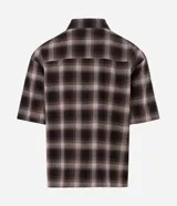 Camisa boxy de manga corta color marrón y negro a cuadros, con cuello camisero que presenta detalle de lettering bordado.