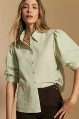 Camisa blanca de manga corta con volumen en los hombros, cuello camisero y cierre frontal con botones dorados.