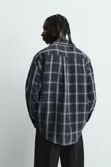 Camisa de corte relajado confeccionada en tejido fluido de cupro y viscosa, con estampado de cuadros, cuello solapa, manga larga con puño abotonado y cierre frontal de botones.