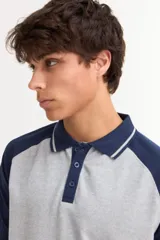 Remera tipo polo de manga corta con diseño combinado, presentando cuerpo en color azul marino y mangas y cuello en color gris. Cuenta con cierre frontal de botones.