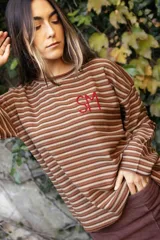 Remerón de manga larga con diseño de rayas horizontales finas en tonos tierra. Presenta un corte holgado y cuenta con un bordado artesanal en color rojo en el pecho.