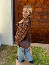 Cartera bandolera de cuero color chocolate con solapa frontal, costuras a la vista y herrajes metálicos. Incluye dos correas desmontables, una corta y una larga, y cuenta con bolsillo interior.