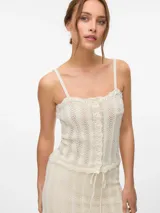 Top tejido de punto calado color crema, con breteles finos, escote cuadrado y cierre frontal con botones. Presenta un diseño ajustado con terminaciones onduladas en el ruedo.