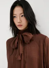 Blusa de viscosa color marrón chocolate, con diseño semitransparente, cuello alto y mangas largas con puños acampanados y volados.