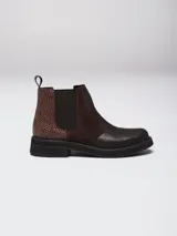 Botinetas tipo Chelsea de cuero marrón, con paneles laterales elásticos y detalle de textura símil reptil en el talón. Poseen suela plana de goma negra y tirador trasero.