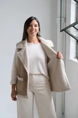 Chaleco de gamuza color beige con interior y detalles de corderito color crudo. Presenta solapas amplias, bolsillos frontales aplicados y diseño sin mangas.