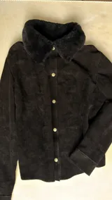 Camisa de cuero negro con cuello de corderito natural, cierre frontal con broches metálicos y puños ajustables.
