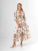 Vestido midi de estilo campesino confeccionado en organdí con estampa floral chintz de estilo romántico. Presenta escote en V cruzado, cintura completamente elastizada y falda larga con volados en niveles. Las mangas son tres cuartos con volados en los puños.