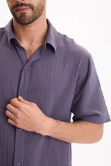Camisa de muselina de manga corta color beige, con cuello camisero y cierre frontal de botones.