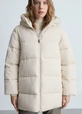 Campera acolchada tipo puffer en color beige, con diseño recto, cuello alto y capucha integrada. Presenta cierre frontal de cremallera doble, mangas largas con puños elásticos y bolsillos laterales con cierre.