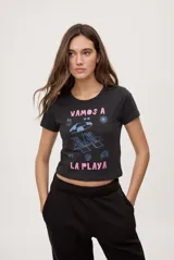 Remera cropped negra de manga corta y calce ajustado, con cuello redondo y estampa frontal que incluye la frase "Vamos a la playa" en tono rosado junto con gráficos veraniegos en celeste.