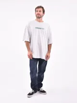 Remera de manga corta color gris claro, corte oversize, con cuello redondo y un pequeño estampado en el pecho con texto en color verde.