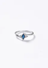 Anillo de plata 925 con diseño de tres piedras, destacando una zirconia central en corte marquesa color azul y dos zirconias laterales pequeñas en corte redondo.