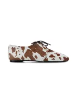 Zapato acordonado de cuero con pelo, estampado con diseño de manchas de vaca en tonos blanco y marrón. Presenta una silueta clásica de perfil bajo con suela plana.