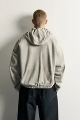 Cazadora de piel de ante color gris oscuro con capucha ajustable, cierre frontal de cremallera bidireccional y bolsillos de vivo en la cadera. Presenta diseño regular fit con acabados elásticos en puños y dobladillo.