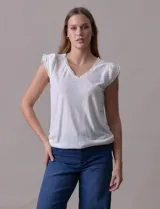 Remera blanca de modal, marca French Laundry, con escote en V. Presenta apliques de puntilla en las mangas y el escote, y un detalle fruncido en los hombros.