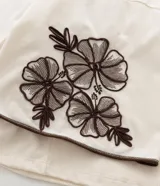 Blusa de corte boxy en color crudo, con cuello redondo y mangas cortas estilo godê. Presenta detalles de bordado floral en tonos marrones en ambas mangas.