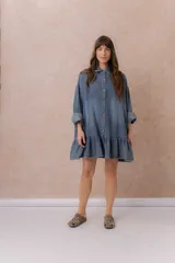 Vestido camisero corto de denim liviano azul con efecto desgastado, de corte oversize, con cuello camisero, botonadura frontal, bolsillo plaqué en el pecho, mangas largas y volado fruncido en el ruedo.