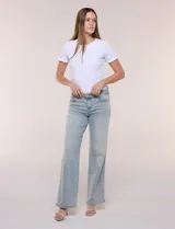 Jean wide leg de tiro medio, color azul claro, confeccionado en denim de algodón con un toque de elastano. Cuenta con cinco bolsillos, presillas para cinturón y cierre frontal con botón. El diseño destaca por su pretina regulable con cruce y broches metálicos.