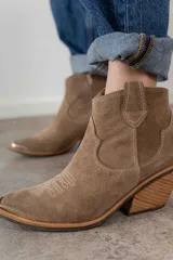 Bota corta de cuero gamuzado color negro, con punta fina y diseño bordado estilo western. Tiene un pequeño tirador en la parte trasera y un taco cónico de altura media.