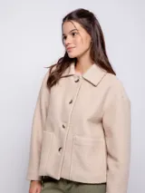 Tapado corto de paño con cuello camisero, cierre frontal de botones veteados y dos bolsillos frontales tipo parche. Presenta un diseño de corte recto y mangas largas.