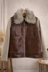 Campera combinada con cuerpo de cuero marrón y mangas de lana en tono beige. Presenta cuello de piel sintética, cierre frontal con cremallera y bolsillos frontales con solapa y hebillas decorativas.