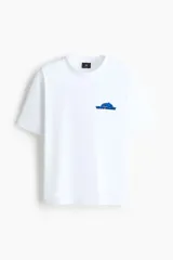 Remera blanca de punto de algodón, cuello redondo, mangas cortas y hombros caídos con pequeño estampado azul en el pecho.
