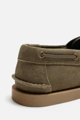 Zapato náutico color verde oliva, confeccionado en cuero serraje, con cordones de cuero y suela plana.