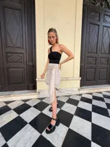 Falda cruzada corta color beige con estampado de lunares negros. Presenta un lazo ajustable en la cintura y un ruedo asimétrico con caída.